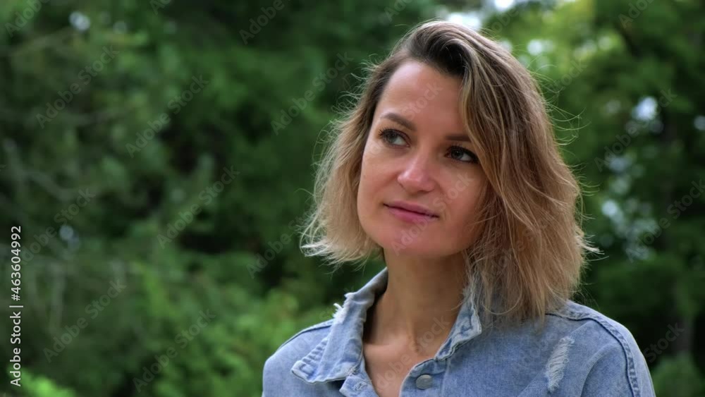 A large head portrait of a Caucasian blonde woman of 35 years in a blue denim jacket against the background of a green forest and nature. Copy space, camera movement. A large head portrait of a Caucasian blonde woman of 35 years in a blue denim jacket against the background of a green forest and nature. Copy space, camera movement.