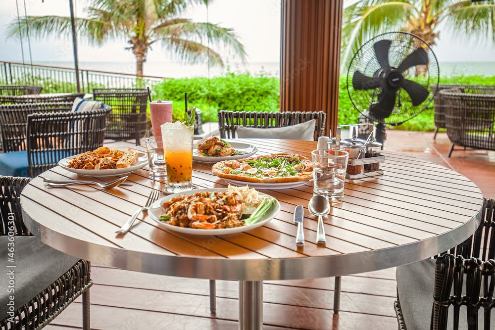 Table with food and cocktails in outdoor restaurant in tropical resort. Italian dishes, pasta, pizza, iced drinks in cafe in hotel on exotic island with palm trees on background. Slow motion.