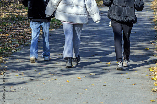 A man and two women walk along the sidewalk on a sunny autumn day