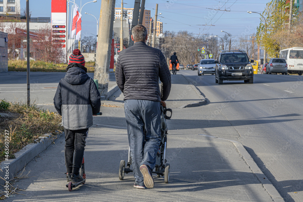 A father walks with two children on the sidewalk on a sunny autumn day