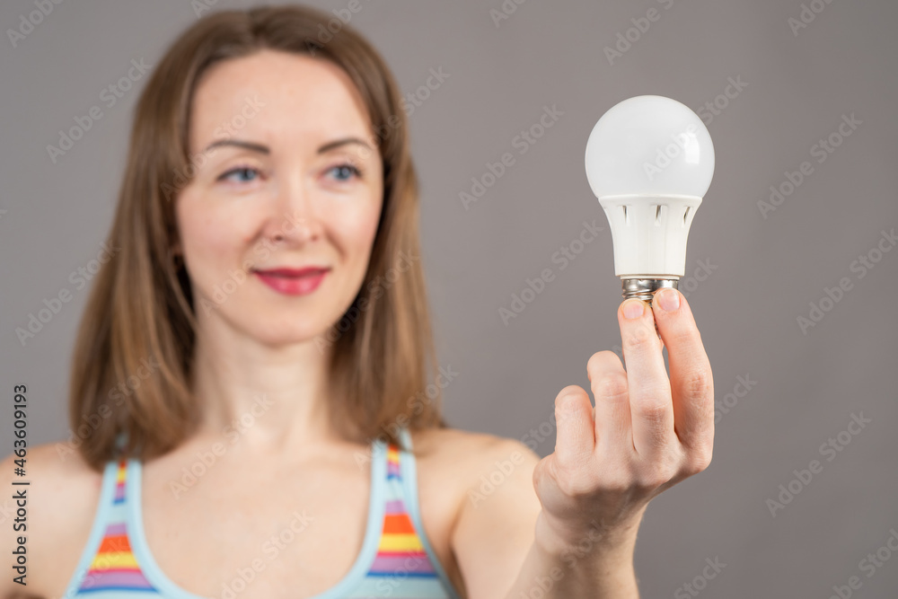 Woman demonstrates an LED light bulb. LED light bulb in hands of a girl. Concept - sale of lighting equipment. Blurred girl in background. Sale of LED lamp. Modern lighting devices. Woman demonstrates an LED light bulb. LED light bulb in hands of a girl. Concept - sale of lighting equipment. Blurred girl in background. Sale of LED lamp. Modern lighting devices.
