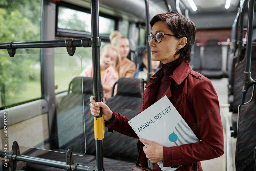 Fototapeta premium Waist up portrait of elegant adult woman holding onto railing in bus while traveling by public transport in city, copy space