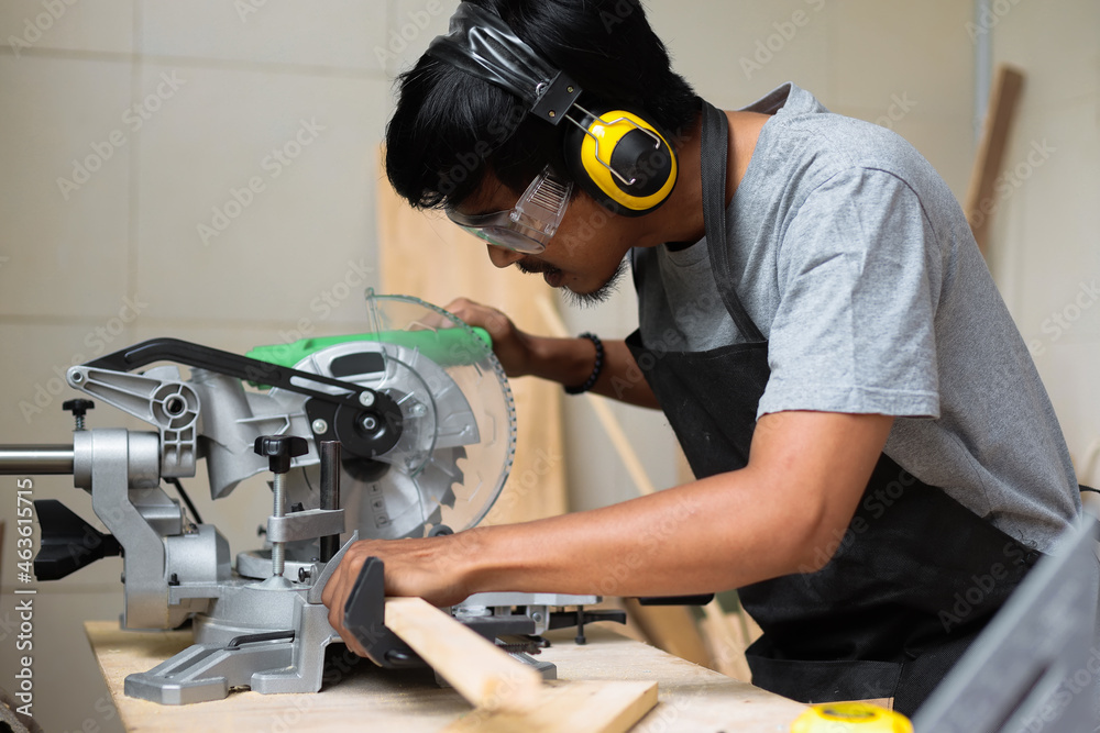 A young male carpenter working on his workshop table using circular saw and wearing safety equipment