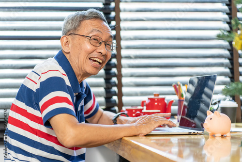 Smiling older man with glasses enjoys learning to use computers and learning how to use social networks to type and send email messages at home.  photo