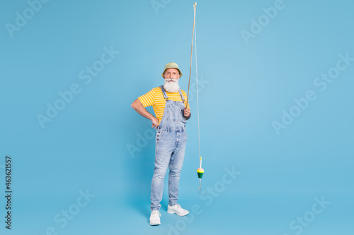 Full length photo of aged man fisherman hold spinning rod sailor isolated over blue color background