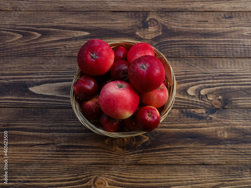 Wicker basket with red ripe apples on rustic wooden table background. Close up of object, top view. Bowl, container with fresh fruits, raw ingredient, natural food. Fall, autumn harvest, thanksgiving