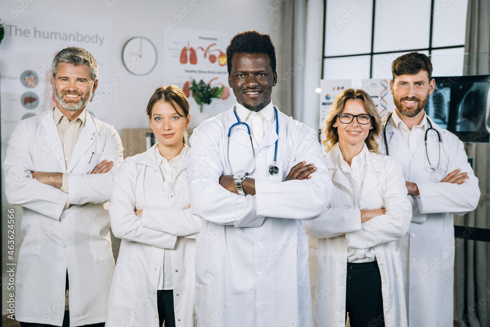Portrait of happy multiracial doctors in medical uniform standing at office room, keeping arms crossed and smiling on camera. Concept of people, medicine and health care. Portrait of happy multiracial doctors in medical uniform standing at office room, keeping arms crossed and smiling on camera. Concept of people, medicine and health care.