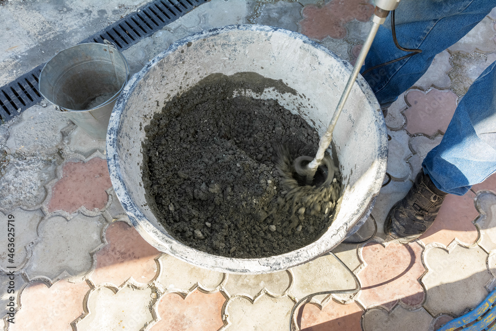 A worker mixes cement and sand to prepare a masonry mortar. Preparatory work for laying paving slabs. A worker mixes cement and sand to prepare a masonry mortar. Preparatory work for laying paving slabs.