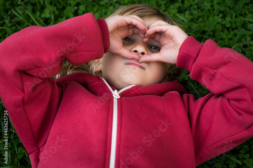 Little cute girl 5 years old blonde in red clothes on the grass, happy childhood.