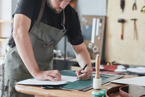 Cropped portrait of male artisan working with leather in tanner workshop, copy space photo