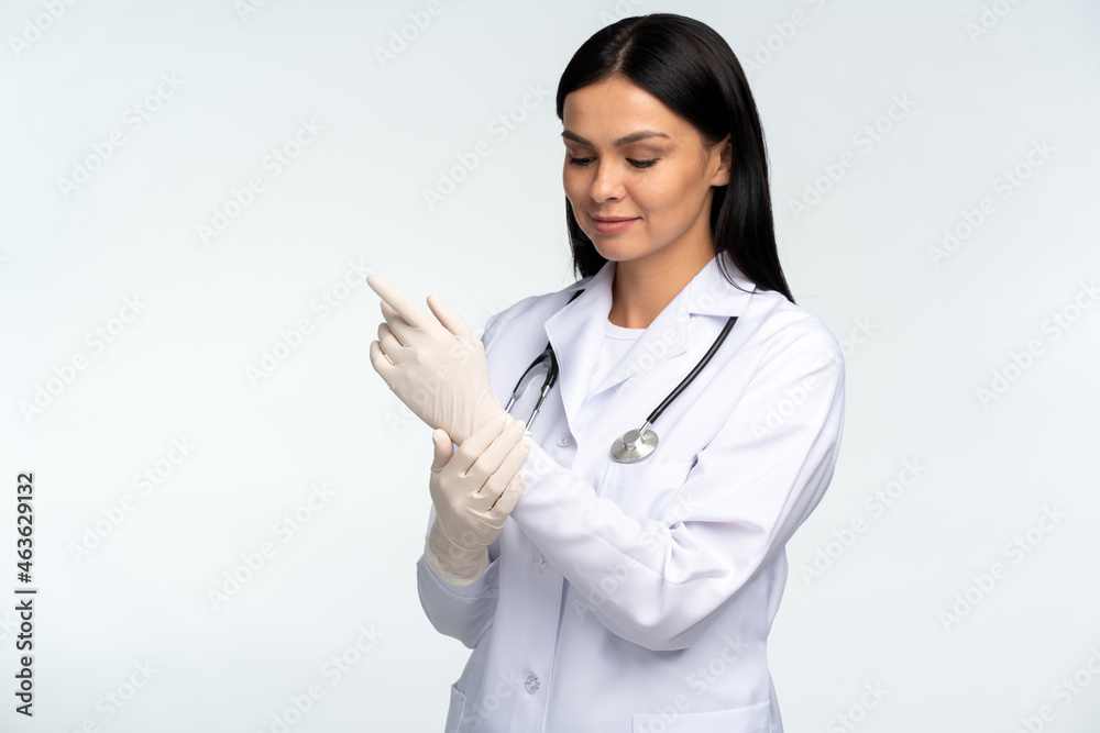 Waist up portrait view of the female doctor putting on medical gloves while preparing to the patient check up isolated over the white background Waist up portrait view of the female doctor putting on medical gloves while preparing to the patient check up isolated over the white background