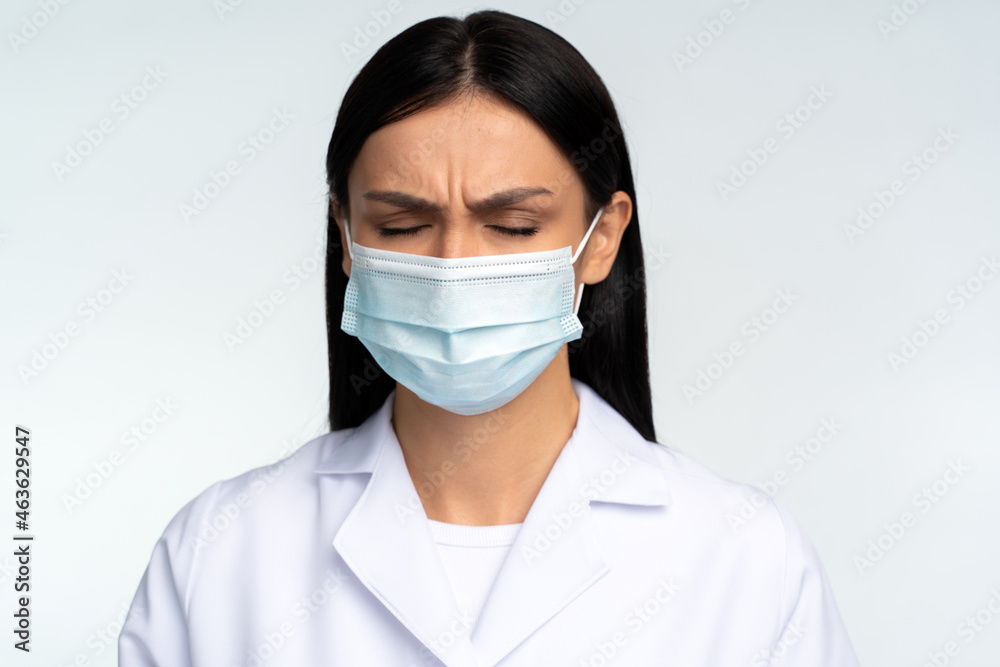 Headache, sadness, confusion or concentration. Portrait of worry alone woman doctor in white suit standing and closed her eyes. Indoor studio shot isolated on white background