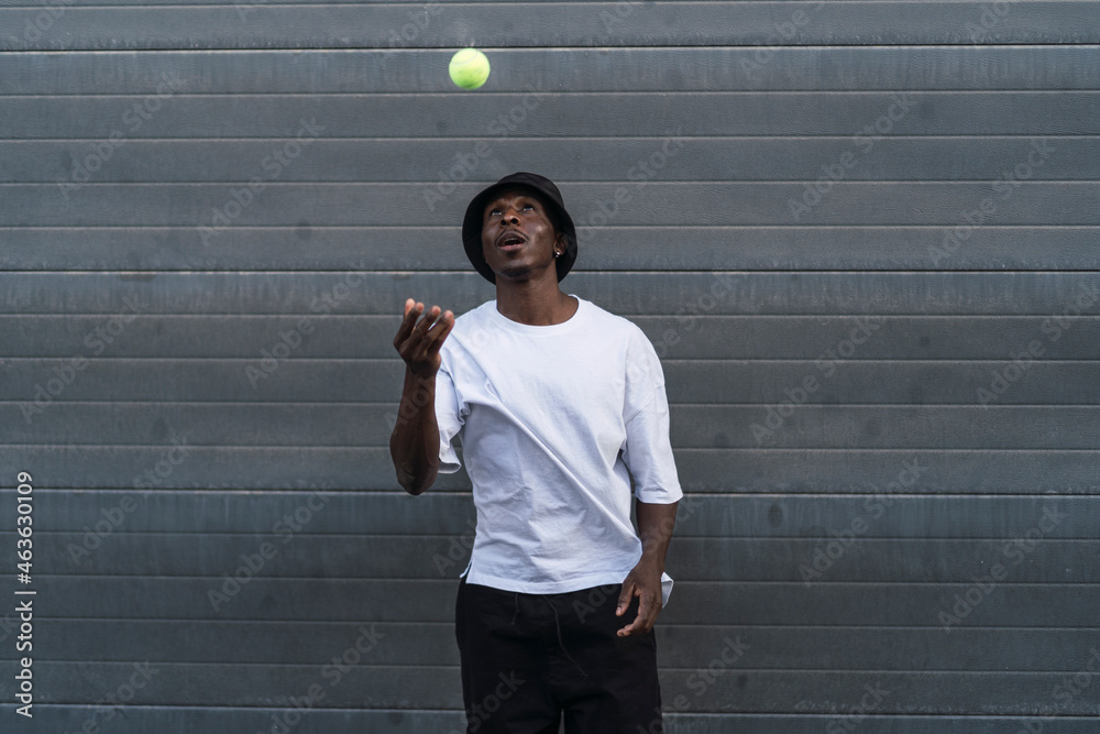 Chico negro con ropa urbana posando con pelota de tenis en pasillo