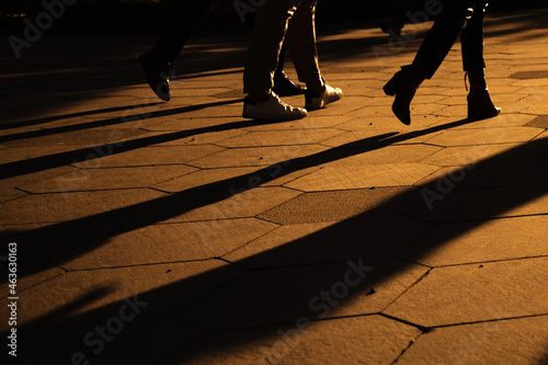 Silhouettes of people legs walking on city street at evening time. Long shadows in golden evening sun. Selective focus.