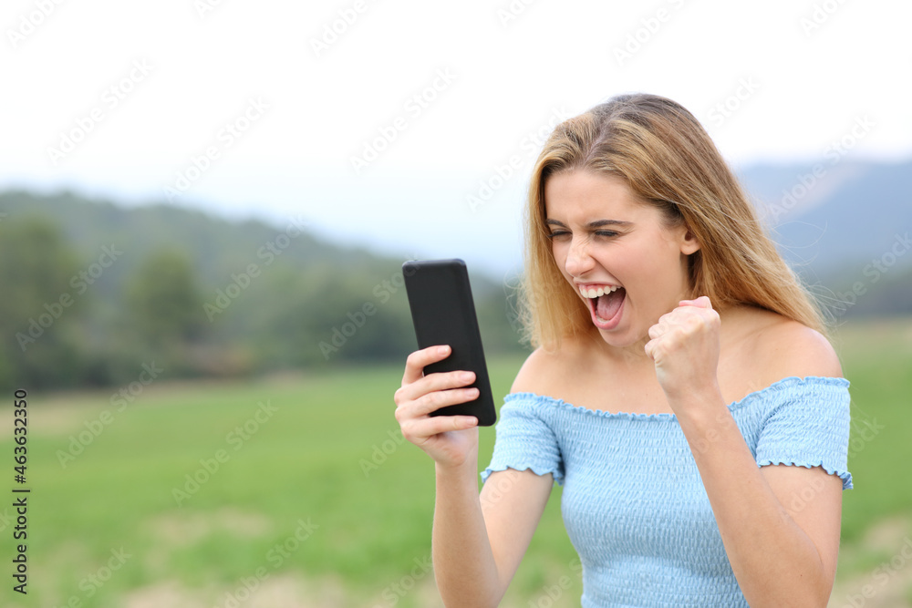 Excited teen checking content on smart phone in a field - obrazy, fototapety, plakaty 