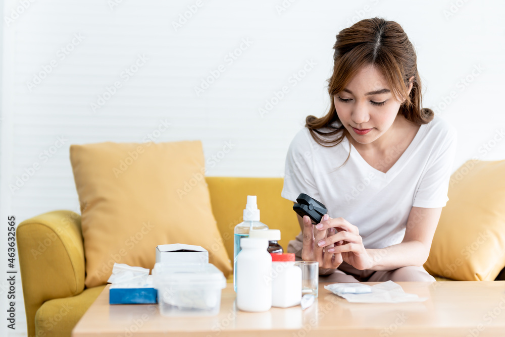 Asian woman, attractive and young Sitting on the sofa, checking her health by using the oxygen level measuring device, with white background, to people and health care concept. Asian woman, attractive and young Sitting on the sofa, checking her health by using the oxygen level measuring device, with white background, to people and health care concept.