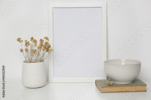 Horizontal white frame mockup on table with books  ceramic vase with yellow dry Everlasting flowers. White wall background.