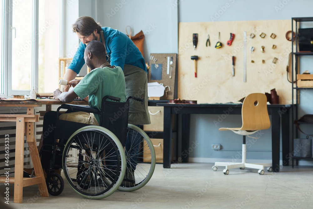 Full length side view portrait of young man in wheelchair learning leathermaking craft in leatherworkers workshop, copy space - obrazy, fototapety, plakaty 