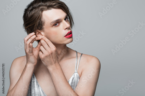 young transgender person touching ear isolated on grey photo