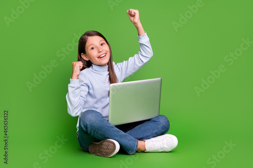 Photo of beautiful lucky girl dressed blue turtleneck communicating modern gadget rising fists empty space isolated green color background © deagreez