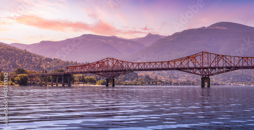 Big Orange Bridge over Kootenay River with Touristic Town in background. Sunrise Sky Art Render. Located in Nelson, British Columbia, Canada. photo