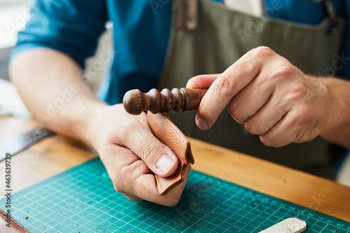 Close up of male artisan finishing leather cardholder in leatherworkers workshop, copy space photo