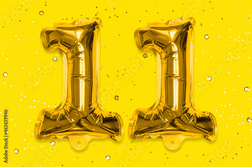 The number of the balloon made of golden foil, the number eleven on a yellow background with sequins. Birthday greeting card with inscription 11. Numerical digit, Celebration event, template. photo