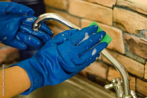 Woman hands in protective rubber gloves wash the faucet with a sponge with foam. Home cleaning concept