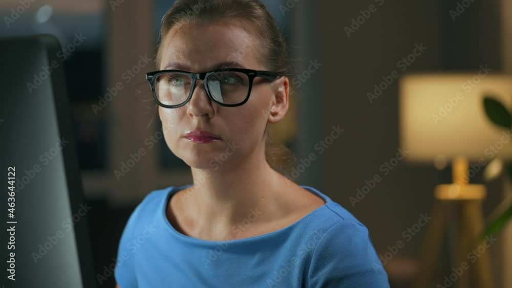 Woman in glasses looking on the monitor and surfing Internet. The monitor screen is reflected in the glasses. Work at night. Home Office. Remote work Woman in glasses looking on the monitor and surfing Internet. The monitor screen is reflected in the glasses. Work at night. Home Office. Remote work