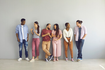 Diverse people leaning on studio background and talking. Full body length indoor group shot of happy young men and women making friends, sharing and listening to opinions and finding common grounds