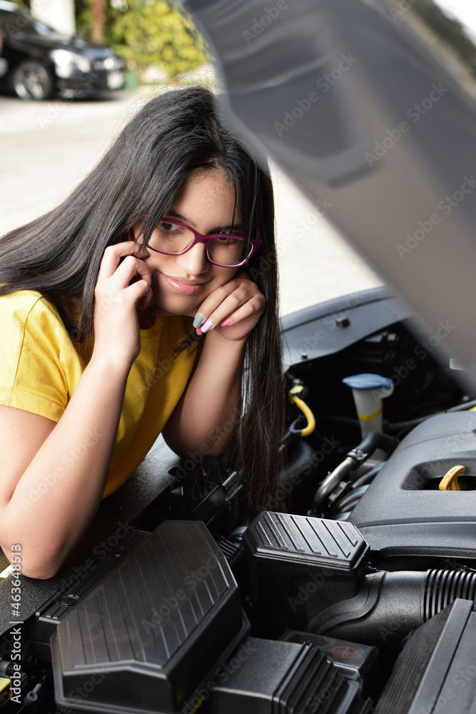 Mujer conductora joven hablando por teléfono con el capo de su auto abierto, esperando por ayuda. Vehículo con problemas. Chica latina con cabello largo hablando por teléfono. Mujer conductora joven hablando por teléfono con el capo de su auto abierto, esperando por ayuda. Vehículo con problemas. Chica latina con cabello largo hablando por teléfono.