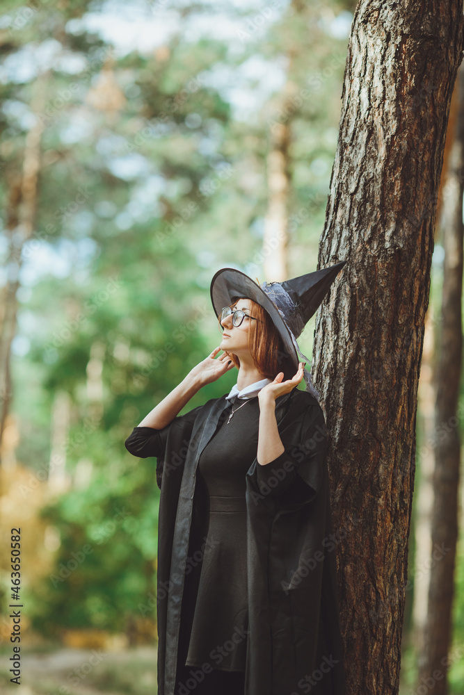 Halloween Witch. Portrait of a girl in a hat and a witch costume in the forest. Ready for trick or treat holiday