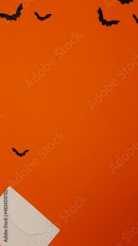 Halloween. A white envelope comes out on an orange background. Black bats fly out of the envelope. Stop motion. Vertical.
