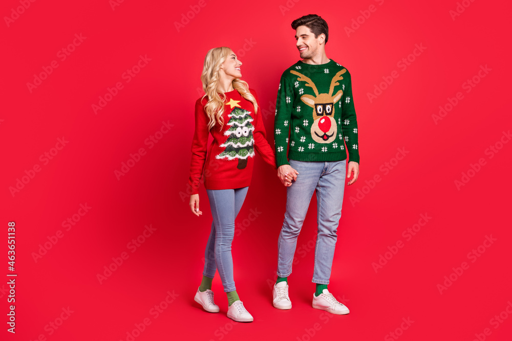 Photo of lover couple hold hands enjoy promenade wear ugly ornament sweater isolated red color background Photo of lover couple hold hands enjoy promenade wear ugly ornament sweater isolated red color background