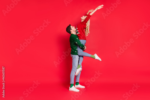 Full length body size photo boyfriend keeping overjoyed happy girlfriend wearing xmas outfits isolated vivid red color background