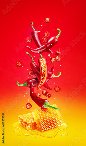Fresh red chilli pepper and sections of chilli pepper floating over honeycombs and honey puddle isolated on red background.