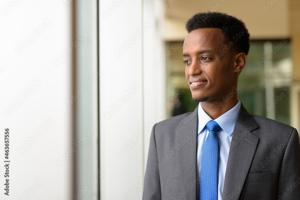 Portrait of handsome African businessman looking through window while thinking Portrait of handsome African businessman looking through window while thinking