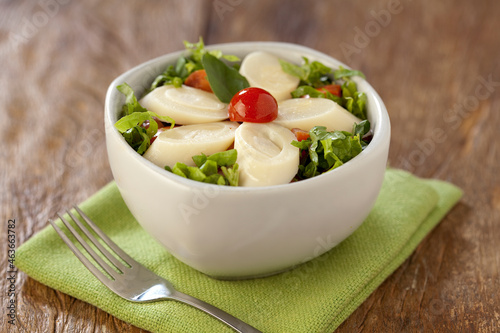 Salada de alface picada com tomate cereja e palmitos fatiados em cumbuca no fundo de mesa rústica. photo