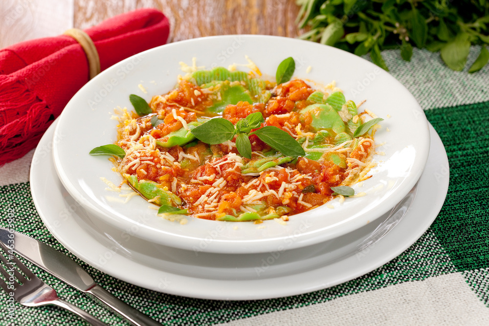 Ravioli verde, massa italiana, com molho de tomate e queijo parmesão e folhas de manjericão. Em fundo de mesa decorada. - obrazy, fototapety, plakaty 
