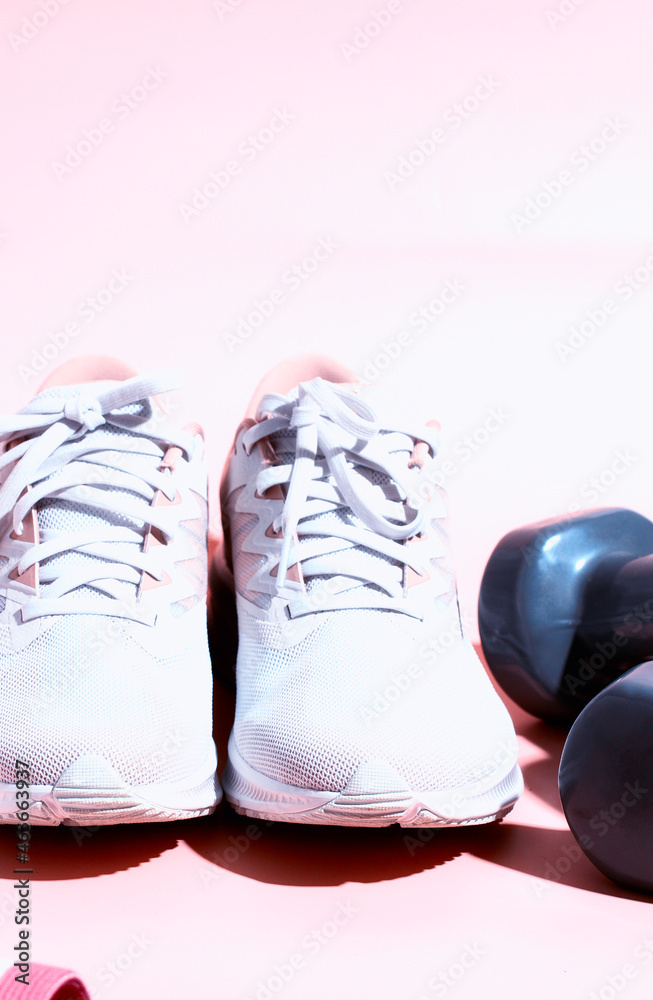 Female sneakers and dumbbells on pink toned background. Essential equipment for sport workout