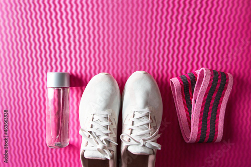 Female fitness concept. Sneakers, booty band,  water bottle on pink exercises mat for  full body workout at home.