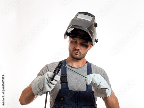 A man with a welding mask on his head, raised up, open face, holding welding wires and an electrode in his hands.