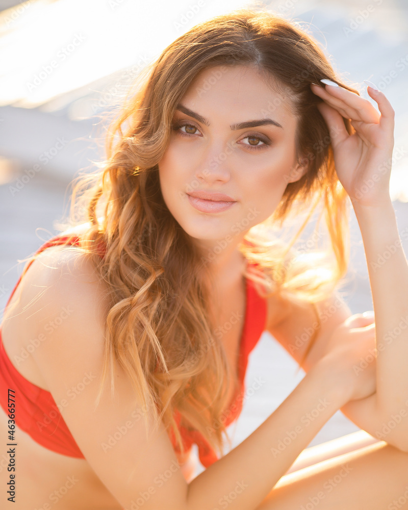 A girl in a red bikini relaxes on the beach in the sunset light