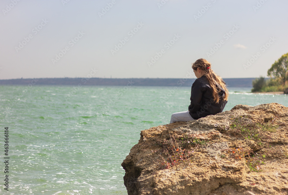 teenage girl sitting on a rock on the bank of the estuary back view