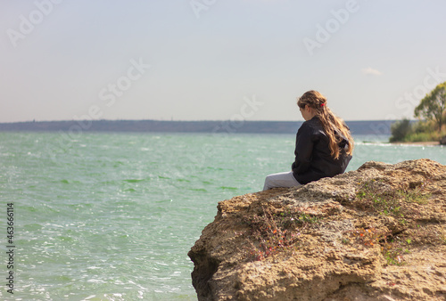 teenage girl sitting on a rock on the bank of the estuary back view