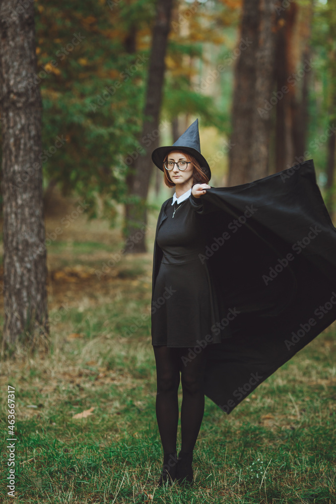 Halloween Witch. Portrait of a girl in a hat and a witch costume in the forest. Ready for trick or treat holiday