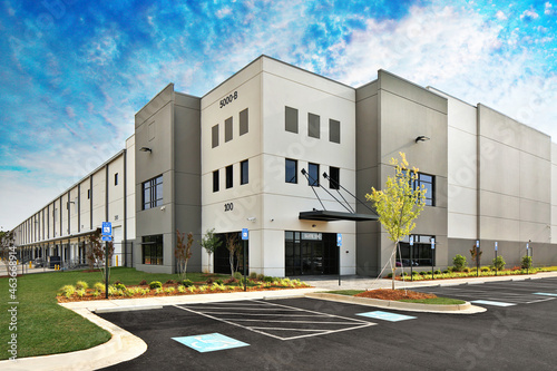 Modern gray warehouse distribution facility and parking lot under gorgeous blue cloudy sky