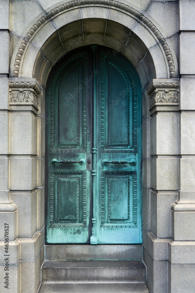 Old, arch, teal iron door to a tomb with ornaments. Door with steps inside the wall