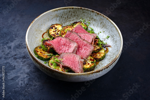 Modern style traditional fried dry aged angus beef filet medaillons with zucchini and cress served as close-up in a Nordic design bowl