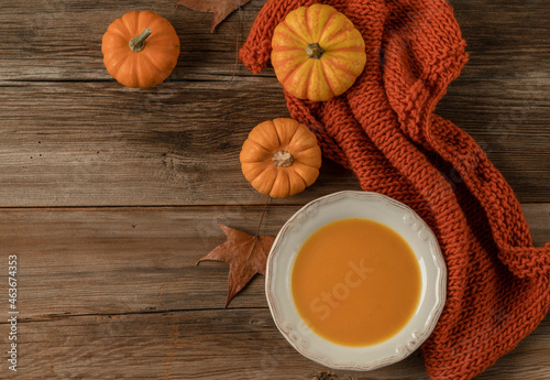 bowl of pumpkin soup on the wooden table decorated with winter squash and autumn leaves